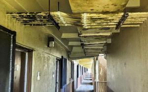 A view of a long concrete corridor with a deteriorating ceiling showing exposed structural elements and water damage.