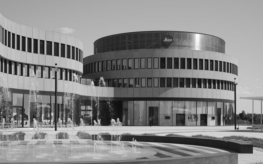 A black-and-white photo of a modern building with a curved glass facade that has a fountain in front of it.