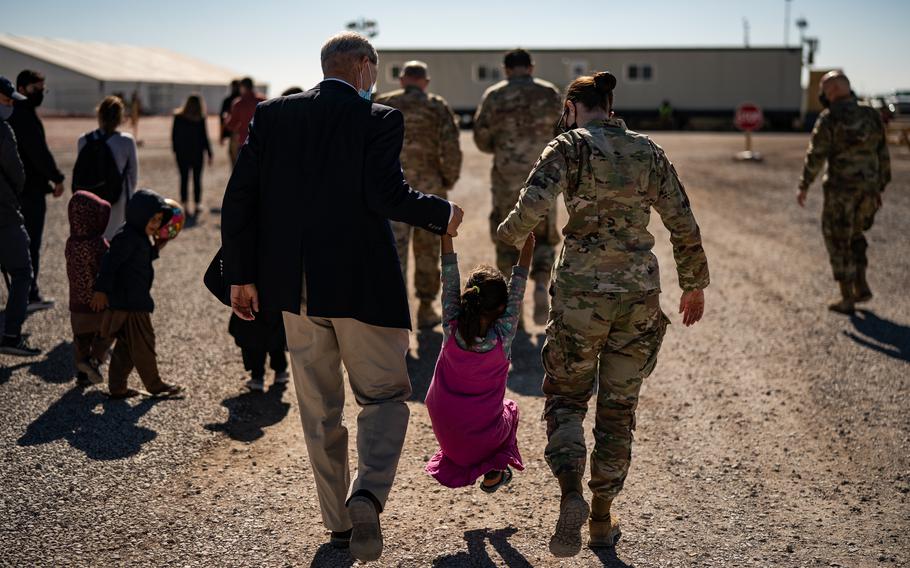 A man plus a woman in uniform each hold the hand of a child and lift her into the air.