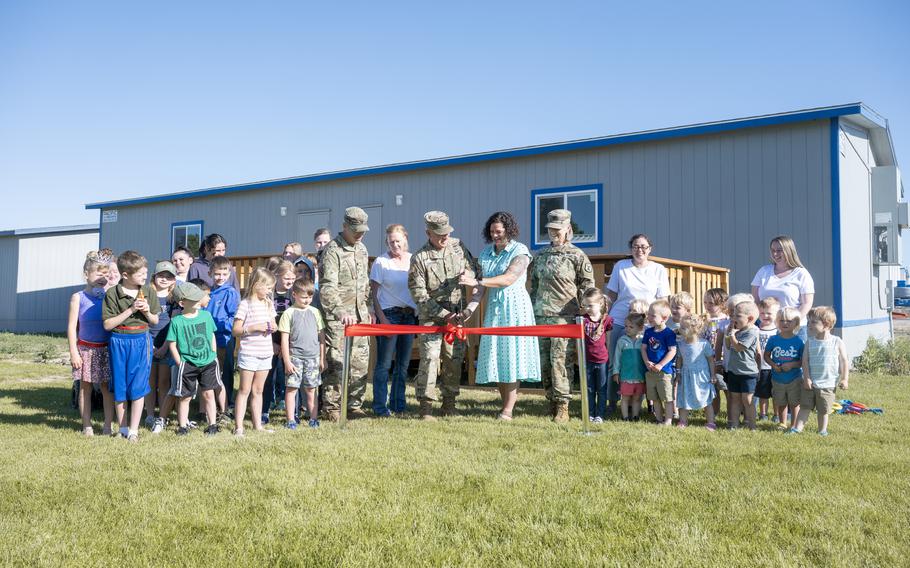 Troops, children and others gather for a ribbon-cutting outside a building.