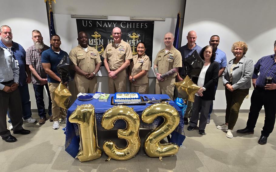 A group of sailors pose for a photo behind balloons that say “132”