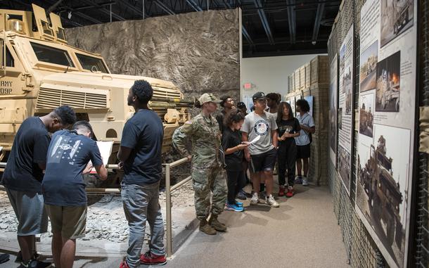 Students walking around a museum exhibit that features a military vehicle.