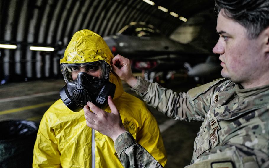 Staff Sgt. Joshua Crenshaw, a bioenvironmental engineering technician with the 52nd Medical Group, right, helps secure the protective hood of Staff Sgt. Michael Tobat, a maintainer with the 480th Fighter Generation Squadron during exercise Radiant Falcon April 24, 2024, at Spangdahlem Air Base, Germany. 