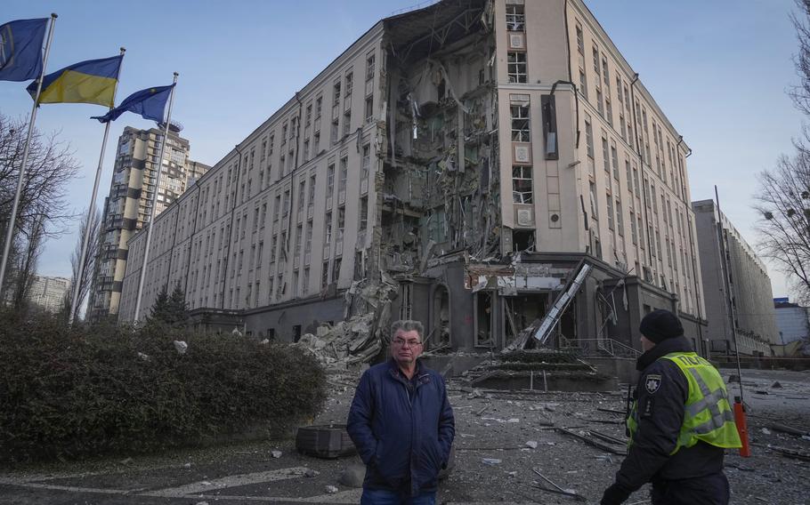 People stand in front of damaged hotel at the scene of Russian shelling in Kyiv, Ukraine, Saturday, Dec. 31, 2022. 