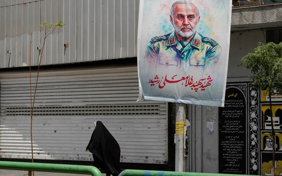 A woman walking down a street with a large, colored poster of a man’s face looming behind her.