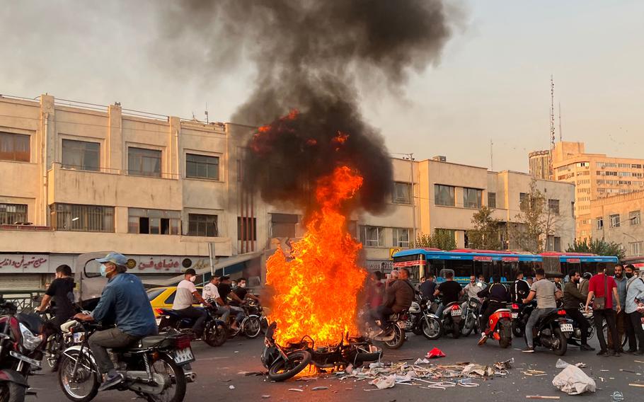 People gather next to a burning motorcycle in the capital Tehran on Oct. 8, 2022. 
