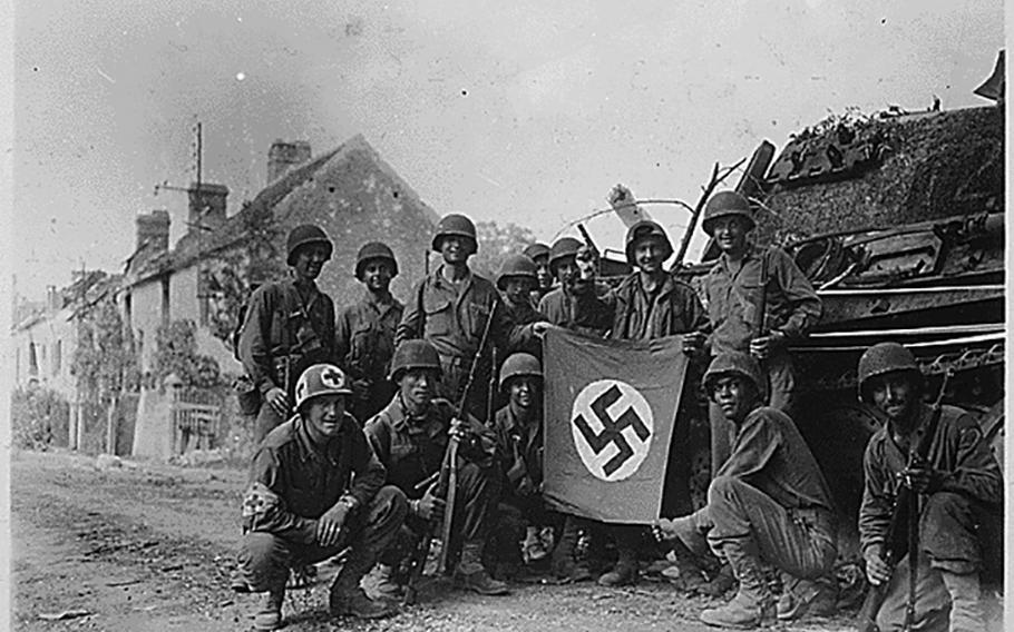 Lined up in front of a wrecked German tank and displaying a captured swastika, is a group of American infantrymen who were left behind to “mop-up” in Chambois, France, last stronghold of the Nazis in the Falaise Gap area.