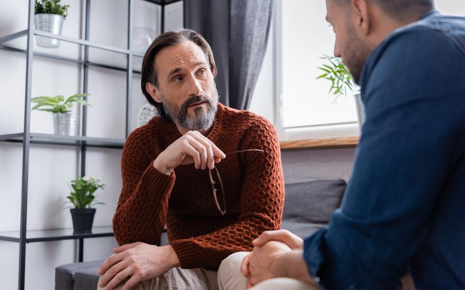 bearded man holding eyeglasses while listening to son on blurred foreground