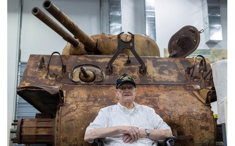 A Marine veteran sits in front of a tank.