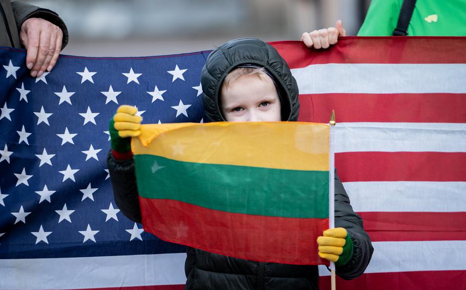 A child with a Lithuanian flag stands in front of an American flag. 