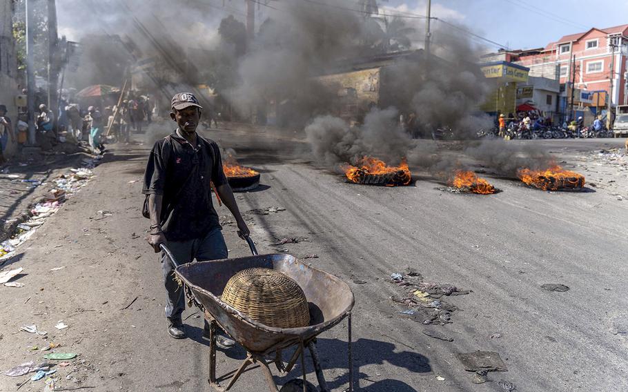 A man pushes a wheelbarrow near burning tires during a day of protest after the deaths of six police officers in Port-au-Prince, Haiti, on Jan. 27, 2023. 