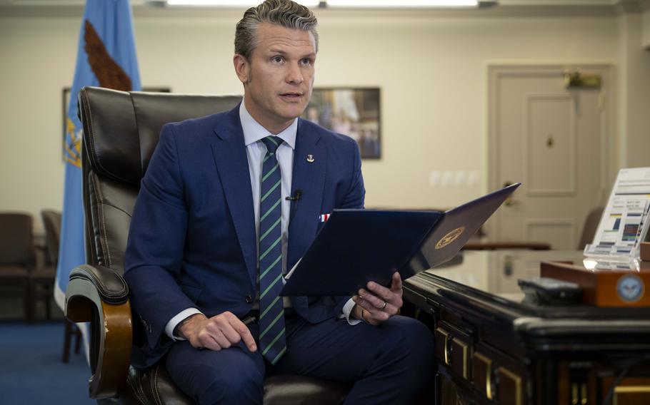Hegseth seated and holding open a folder. 
