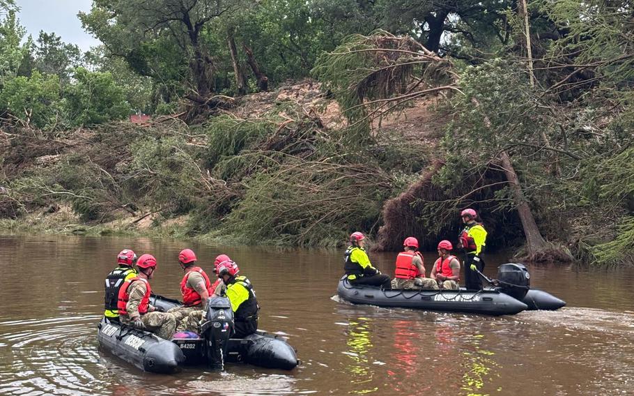 Troops on motorized rafts search a river.