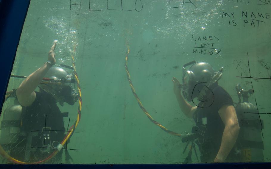 Two Navy divers raise their hands underwater