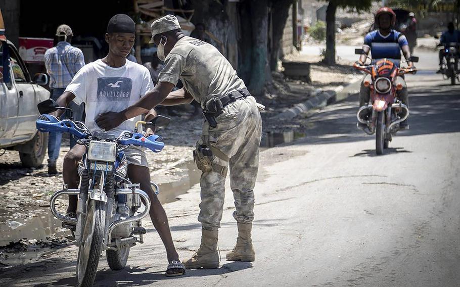 A Haitian Policeman frisks a motorcyclist at a check point on June 23, 2022, in Butte-Boyer 75, where a deadly gang war erupted in late April. Police launched a military style incursion to take back the key intersection. 