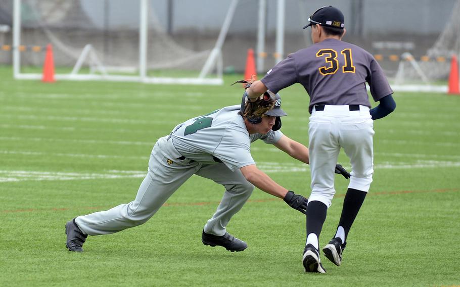 American School In Japan’s Billy Freund tries to tag Kubasaki’s Skylar Waltz diving back to first base during Friday’s inter-district baseball game. The Dragons edged the Mustangs 2-1.
