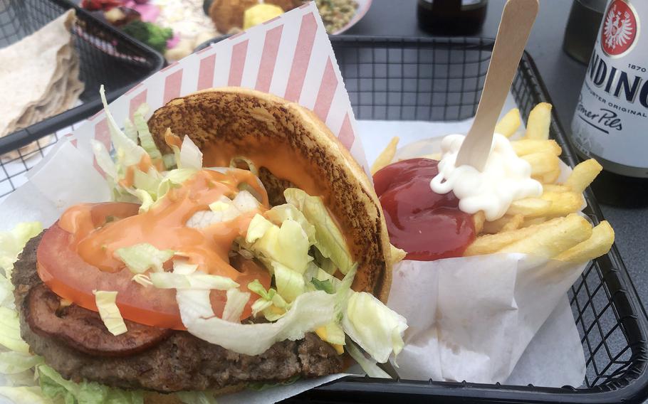 A bacon cheeseburger with fries as served at Hamburger am Turm in Frankfurt, Germany. In the background is a vegetarian falafel plate with various salads. One of the beers offered is from the local Binding brewery.