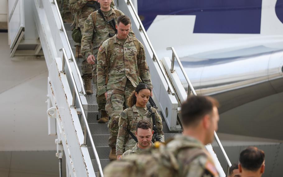 Soldiers in camouflage uniforms descend a staircase to get off an airplane.
