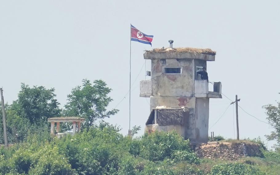 A soldier stands at a North Korean military guard post flying a national flag.