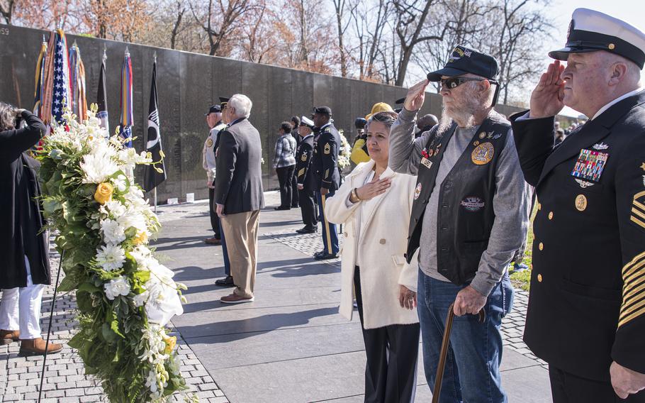 Carrol “Buzz” Izard, Gold Star son of Master Sgt. B.C. Izard, salutes during the playing of Taps on National Vietnam War Veterans Day at the Vietnam Veterans Memorial in Washington, D.C., on Wednesday, March 29, 2023. Also saluting at right, is Master Chief Petty Officer of the Navy James Honea, and his wife, Evelyn, at left, placing her hand over her heart.