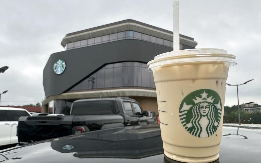 An iced latte in a plastic Starbucks cup sits on a car in front of Starbucks in Korea.