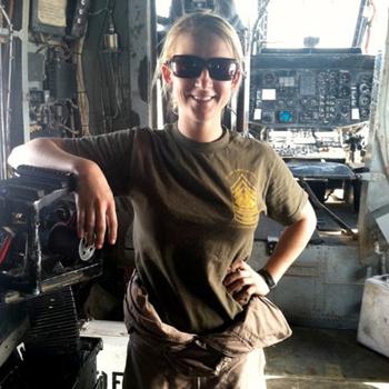 A woman in a green Marine t-shirt and sunglasses poses in a military helicopter.