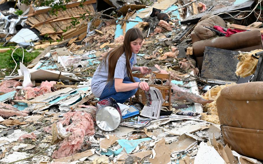 A woman in jeans and T-shirt kneels down among the debris of a detroyed home.