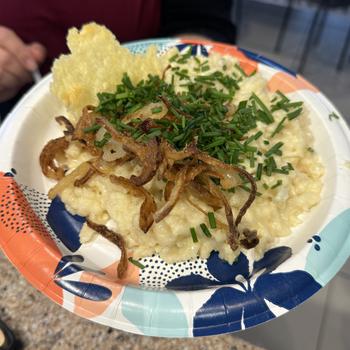 Cooked Kaesespaetzle on a paper plate topped with chopped chives and fried onions