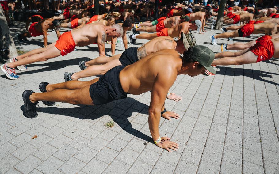Participants in bright orange and black swim trunks complete 100 pushups at Battery Park in New York City.