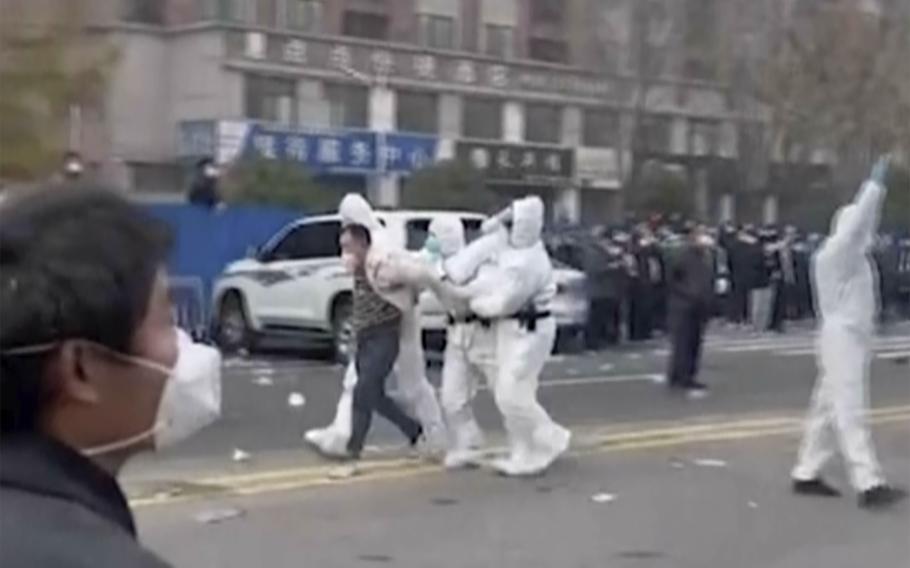 In this photo provided Nov 23, 2022, security personnel in protective clothing were seen taking away a person during protest at the factory compound operated by Foxconn Technology Group who runs the world's biggest Apple iPhone factory in Zhengzhou in central China's Henan province. Employees at the world's biggest Apple iPhone factory were beaten and detained in protests over pay amid anti-virus controls, according to witnesses and videos on social media Wednesday, as tensions mount over Chinese efforts to combat a renewed rise in infections.