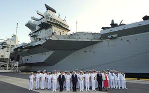 A group of British sailors at a dock next to an aircraft carrier.