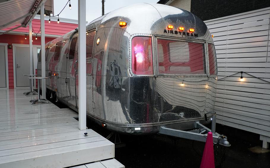 A shiny silver Airstream travel trailer is parked next to a deck.