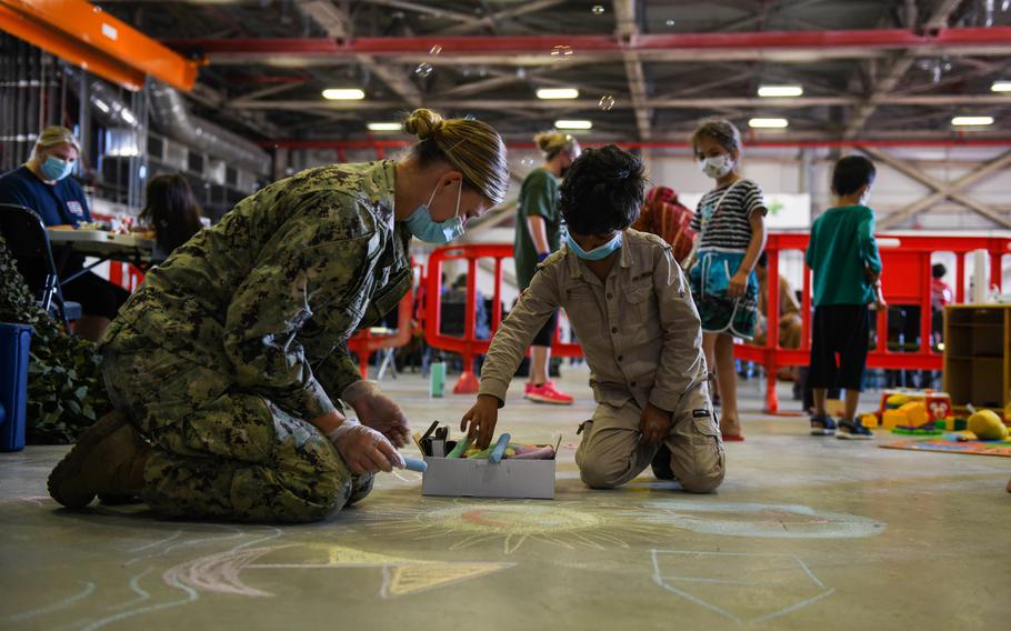 A U.S. sailor plays with a child evacuated from Afghanistan as they wait to check in after arrival at Naval Air Station Sigonella in Italy on Aug. 27, 2021.