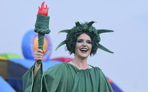 A woman dressed as the Statue of Liberty holds up a prop torch during an outdoor festival.