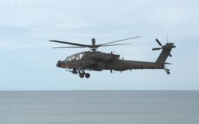 An Army AH-64E Apache helicopter flies over water.