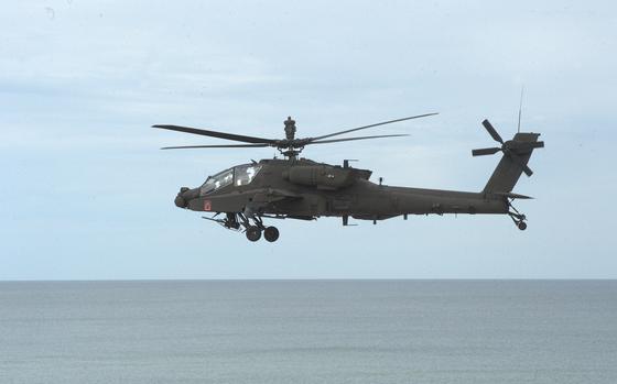 An Army AH-64E Apache helicopter flies over water.
