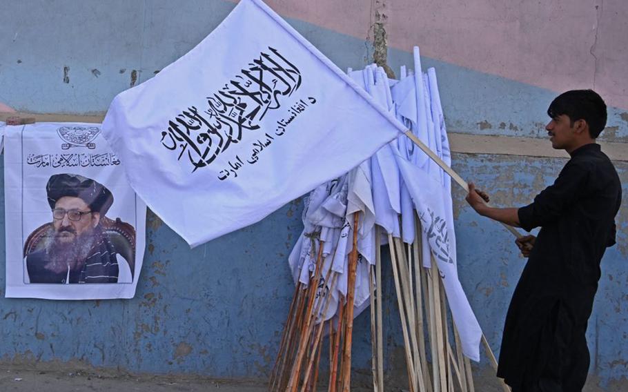 A vendor holds a Taliban flag next to a poster of Taliban leader Mullah Abdul Ghani Baradar as he waits for customers along a street in Kabul on August 27, 2021, following the Taliban's military takeover of Afghanistan. 