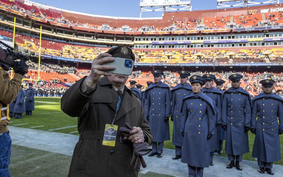 A soldier takes a selfie on the field with cadets in the background.