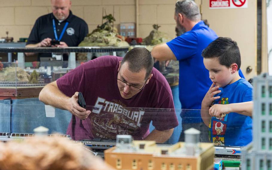A man shows a child how to operate a model train with a phone app. 
