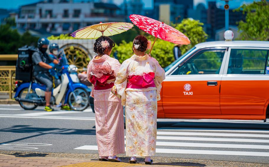 Two kimono-clad women wait to cross a street in Kyoto, Japan, May 28, 2025.