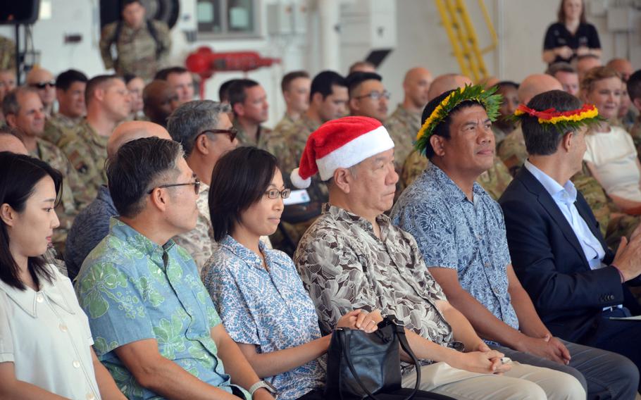 A crowd, with some wearing flower crowns and one man wearing a Santa hat, sits at Andersen Air Base.