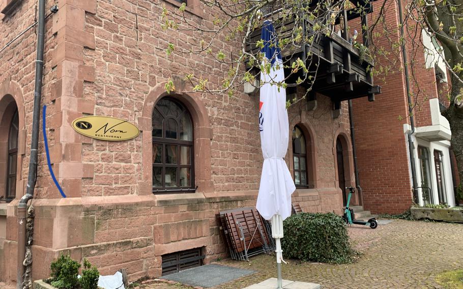 A closed umbrella and folded up tables out behind Nora Restaurant, in downtown Kaiserslautern, await warmer weather, April 1, 2022.