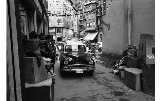 Andorra la Vella, Andorra, Sep. 1962: A car and its driver maneuver through the narrow streets in Andorra la Vella, Andorra, careful not to hit the people to the right of him or the goods to the left. Nestled in the Pyrenees mountains and close to the Spanish border, the city is the capital of the small Principality of Andorra. The tax-free principality is a shopping haven for many tourists flocking from neighboring Spain and France.

Check out Stars and Stripes' Europe Community site for travel articles on Andorra [https://europe.stripes.com/search/node?search-results=andorra]

METATAGS: Europe; Andorra; city; street; tourism; culture; locals; Andorrans; tourists; automobile