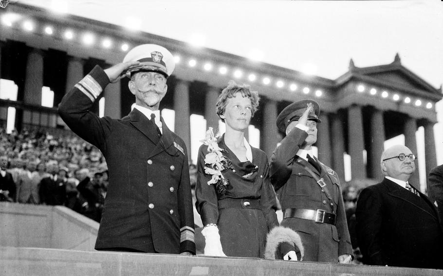 Rear Adm. Walter Crosley, from left, Amelia Earhart and Maj. Gen. Frank Parker salute the flag on the reviewing stand at the George Washington bicentennial military tournament held at Soldier Field on June 24, 1932.