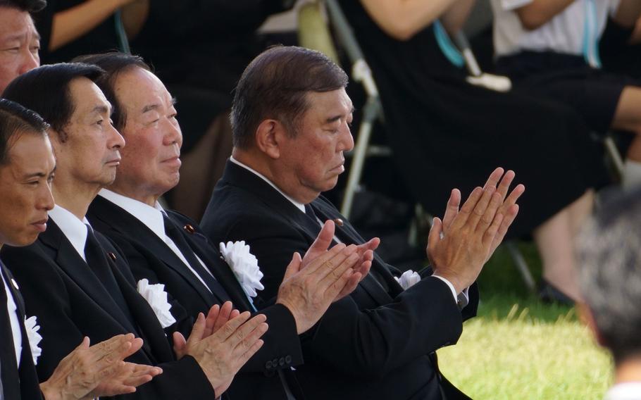 The Japanese prime minister claps while sitting in a row with other men.