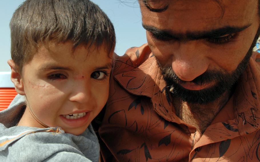 Saleh al-Assadi and his 4-year-old son, Mahdi, wait at the gates of an American base near Basra, Iraq, Nov. 18, 2009. Mahdi was injured when an insurgent mortar attack struck his house. Soldiers helped get him get medical care locally, followed by surgery overseas. They remain in contact with a veteran who first helped them.