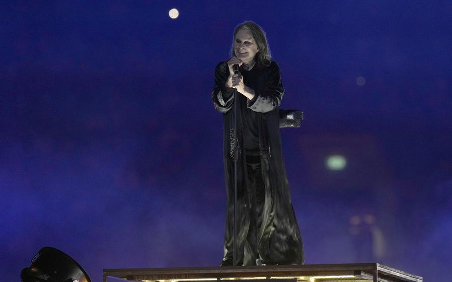 A man in black robes performs on stage holding a microphone.