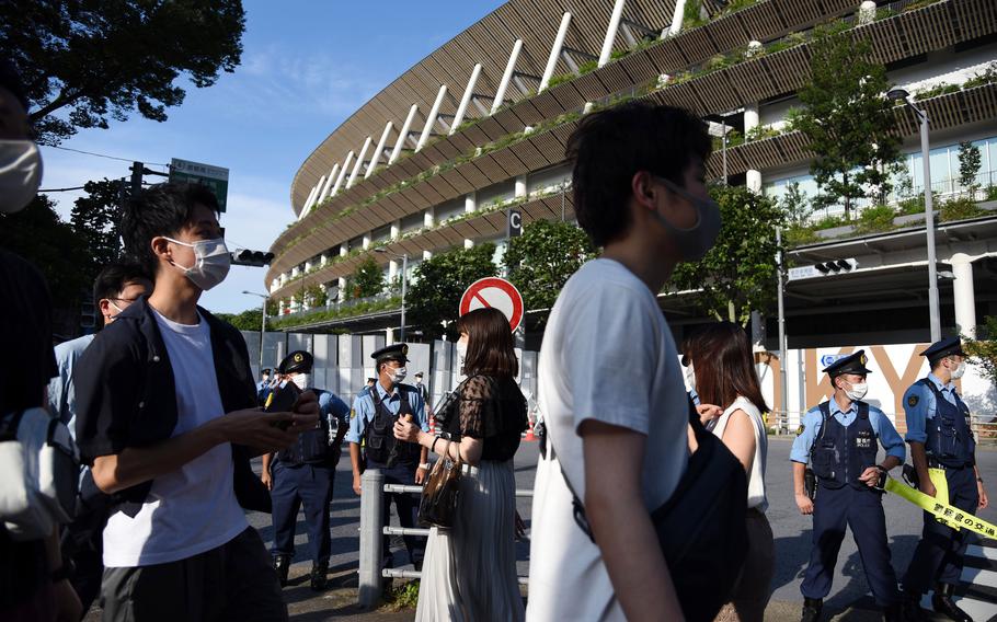 People in masks gawk at the new National Stadium hours before the opening ceremony for the pandemic-delayed Tokyo Olympics, Friday, June 23, 2021. 