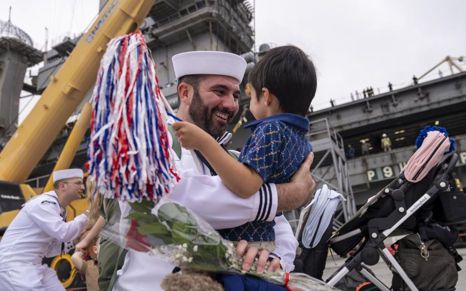A sailor holds a child and smiles.