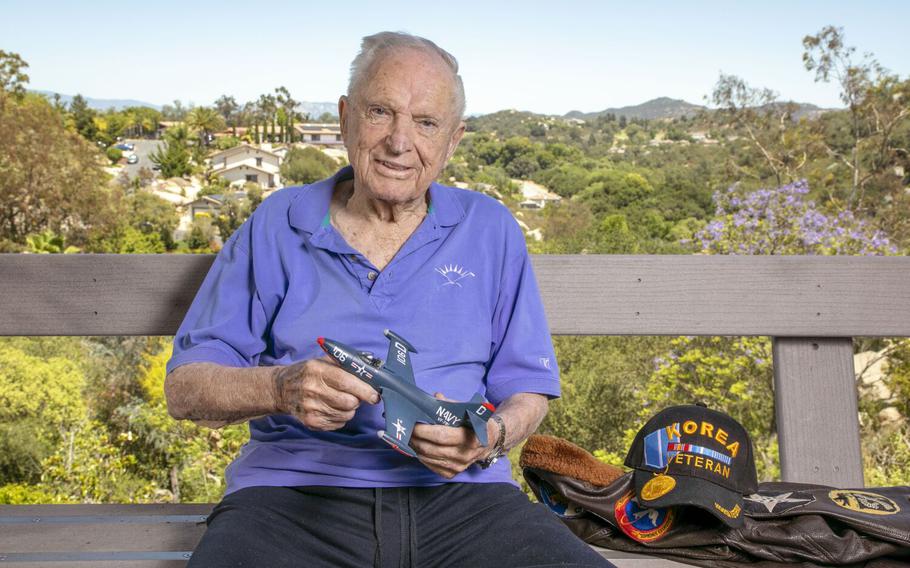 Veteran Royce Williams, 97, sits on his patio overlooking a canyon in the Mountain Meadows area of Escondido, Calif., on June 13, 2022. He’s holding a model of the Navy F9F-5 Panther jet he flew in an aerial dogfight in the Korean War. 